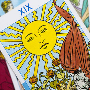 The image shows the Sun tarot card, featuring a bright yellow sun with a face at the top, radiating sunbeams. Below are four sunflowers and a child riding a white horse. The card is labeled with the Roman numeral XIX.