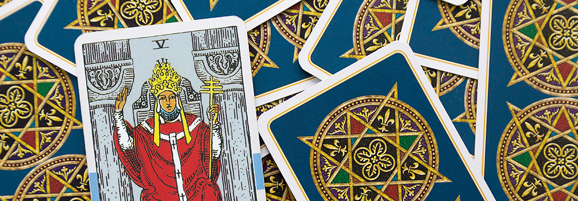 A tarot card featuring The Hierophant is displayed prominently among a scattered deck with ornate gold and blue back designs. The Hierophant card illustrates a figure in red robes holding a staff, symbolizing spiritual authority and guidance.