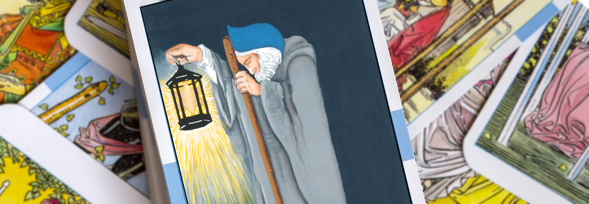 A Tarot card featuring an elderly figure in a cloak holding a lantern and staff. The background is dark, and the card is surrounded by other colorful Tarot cards.