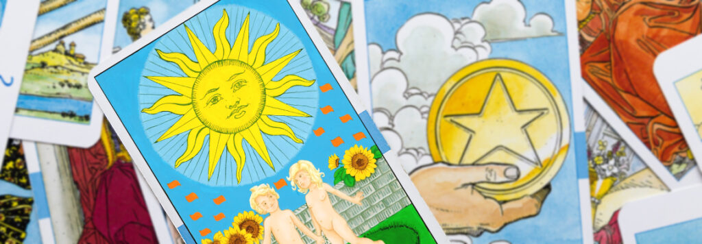 A tarot card featuring a radiant sun with a smiling face, above two children, is prominently displayed. In the background, various other tarot cards are scattered, displaying different mystical symbols and imagery.