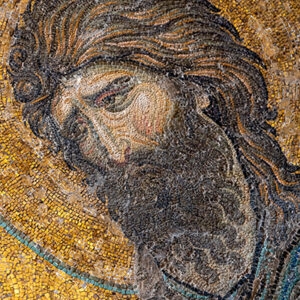 A detailed mosaic of a man with long hair and a beard, set against a golden background. The mosaic features intricate tiles in various shades of brown, gold, and black, creating a sense of depth and texture.