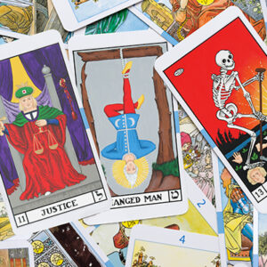 A close-up of tarot cards, featuring Justice, The Hanged Man, and Death cards prominently displayed on top of a scattered pile of various other tarot cards.