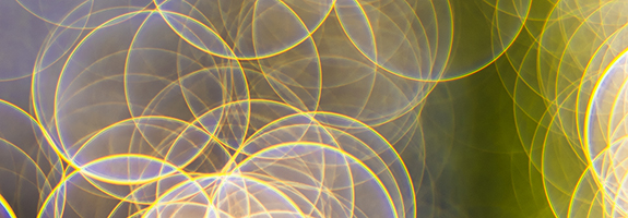 Abstract image featuring overlapping translucent circles of light in yellow and white tones, evoking a sense of meditation, set against a blurred green and purple background with a textured black pattern on the right side.