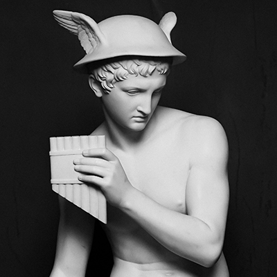 A white marble statue of a young man wearing a winged helmet, holding a pan flute in his right hand against a dark background.